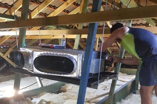 A man installing a ducted aircon unit in ceiling space